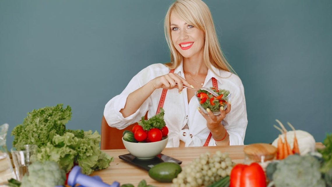 Blonde woman enjoying a fresh salad surrounded by vegetables, promoting healthy eating.