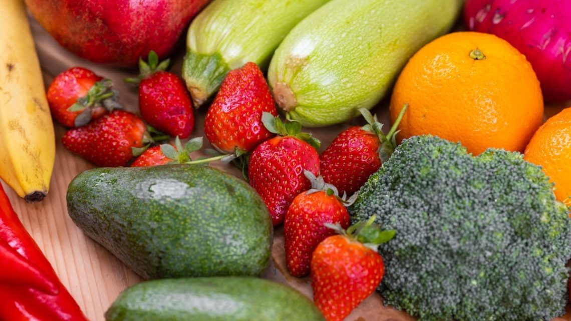 A vibrant selection of fresh fruits and vegetables including strawberries, avocado, and broccoli on a wooden table.
